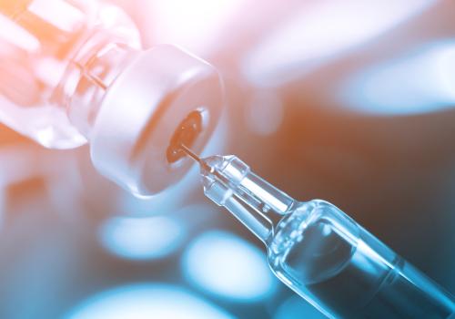syringe needle inserted into vaccine bottle