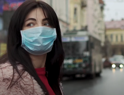 A person wearing a medical mask stands on a street